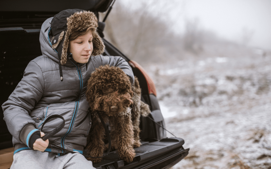 winter weather tips for dogs - a boy and a dog at the back of a car while it is snowing